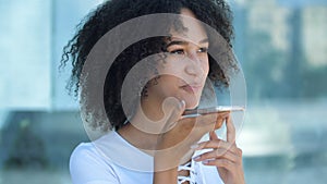 African American girl holding smartphone in hands, talking on speakerphone with friends, smiling, remote communication