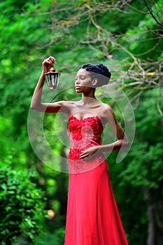 African American girl in a red dress, with dreadlocks, with a lamp and a candle in his hand, stands in the Park in the summer