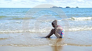 An African-American girl is sitting alone on the beach with lonely emotions.