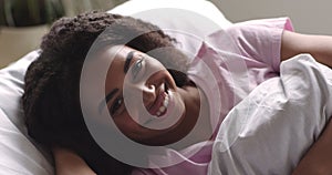 African American girl smiling at camera, lying in bed