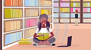 African american girl student sitting lotus pose reading book near bookshelf modern library interior education knowledge