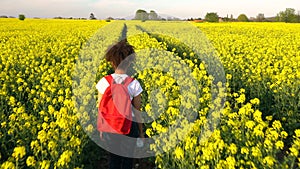 African American girl teenager female young woman hiking with red backpack in field of seed yellow flowers