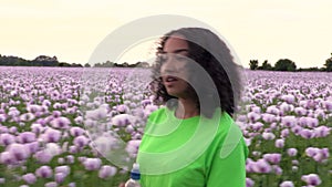 African American girl teenager female young woman walking through field of pink poppy flowers drinking water from a plastic bottle