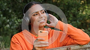 African American girl teenager young woman listening to music on her smartphone or cell phone wearing wireless headphones and drin