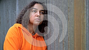 African American girl teenager young woman looking sad or thoughtful wearing an orange hoodie in an urban city environment
