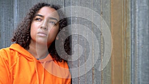 African American girl teenager young woman looking sad wearing an orange hoodie in an urban city environment