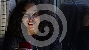 African American girl teenager young woman teen by a window using her mobile cell phone for social media