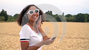 African American girl teenager young woman walking in a field listening to music on her cell phone and wirelesss headphones