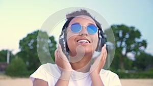 African American girl teenager young woman walking in a field listening to music on her cell phone and wirelesss headphones