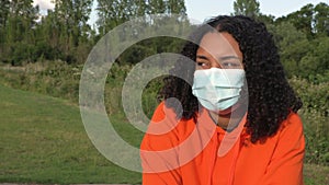 African American girl teenager young woman wearing a face mask during COVID-19 Coronavirus pandemic in an outdoor park