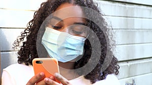 African American girl teenager young woman wearing a face mask during COVID-19 Coronavirus pandemic using her smartphone