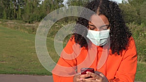 African American girl teenager young woman wearing a face mask during COVID-19 Coronavirus pandemic using her smartphone