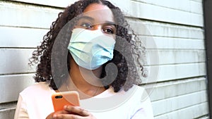 African American girl teenager young woman wearing a face mask during COVID-19 Coronavirus pandemic using her smartphone