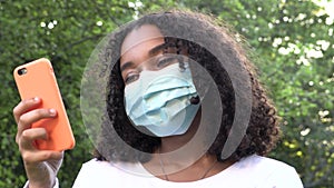 African American girl teenager young woman wearing a face mask during COVID-19 Coronavirus pandemic using her smartphone