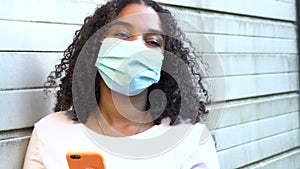 African American girl teenager young woman wearing a face mask during COVID-19 Coronavirus pandemic using her smartphone