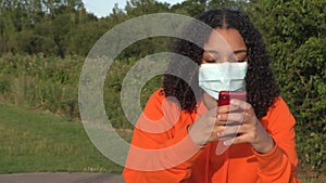 African American girl teenager young woman wearing a face mask during COVID-19 Coronavirus pandemic using her smartphone