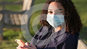 African American girl teenager young woman wearing a face mask using her smartphone or cell phone for social media