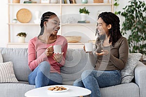 African american girlfriends enjoying weekend together, drinking coffee on couch