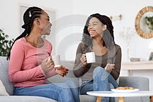 African american girlfriends enjoying weekend together, drinking coffee on couch