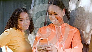 African American girls teenagers, young women outdoors in the city using a smartphone or cell phone for social media