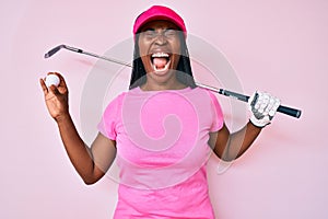 African american golfer woman with braids holding golf ball angry and mad screaming frustrated and furious, shouting with anger