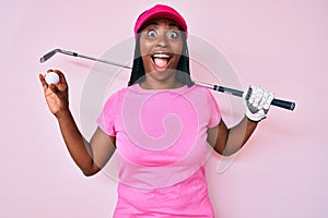 African american golfer woman with braids holding golf ball celebrating crazy and amazed for success with open eyes screaming