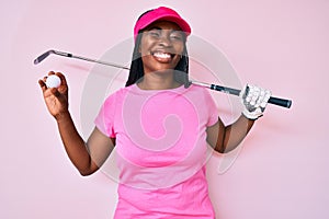 African american golfer woman with braids holding golf ball winking looking at the camera with sexy expression, cheerful and happy