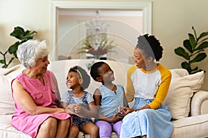 African american grandmother, mother and two granddaughters smiling looking at each other at home