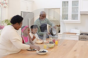 African american grandparents cooking with smiling grandson and granddaughter in kitchen