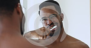 African american guy brushing healthy white teeth looking in mirror