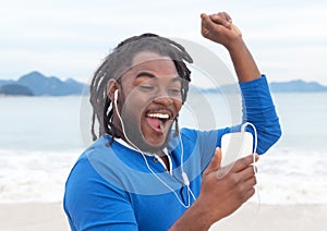 African american guy with dreadlocks listening to music at beach