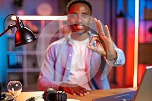 African american guy, working on computer at home and looking at camera showing okay sign