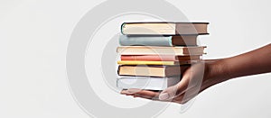 African American hand holding stack of hardcover books. Collection of old books in black female hand. White background