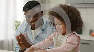 African American happy dad support little child girl daughter kid cooking with flour dough father clapping hands