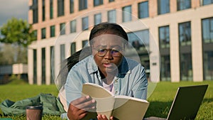 African American happy woman university college academy student teen girl high school lying on green grass in park