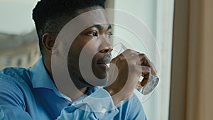 African american healthy man drinking water glass of cold fresh drink sit at home office feel thirsty hydrate body