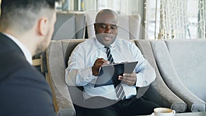 African american HR manager having job interview with young man in suit and watching his resume application in modern