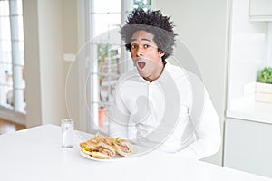 African American hungry man eating hamburger for lunch afraid and shocked with surprise expression, fear and excited face