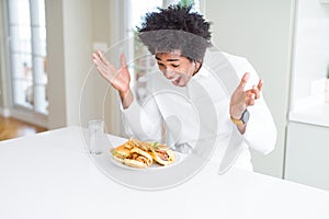 African American hungry man eating hamburger for lunch celebrating crazy and amazed for success with arms raised and open eyes