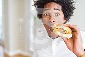 African American hungry man eating hamburger for lunch scared in shock with a surprise face, afraid and excited with fear