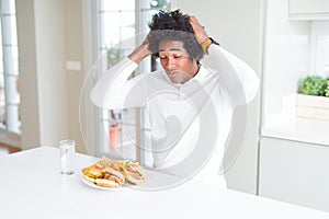 African American hungry man eating hamburger for lunch suffering from headache desperate and stressed because pain and migraine