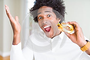 African American hungry man eating hamburger for lunch very happy and excited, winner expression celebrating victory screaming