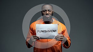 African-american imprisoned male holding punishment sign in cell, human rights