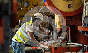 African American industrial worker is using hydraulic power press machine to make metal and steel part while working inside the