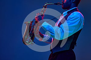 African-American jazz musician playing saxophone his major melodies against blue background in mixed pink-purple