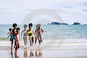 African American, Kids group in swimwear enjoying running to play the waves on beach. Ethnically diverse concept. Having fun after