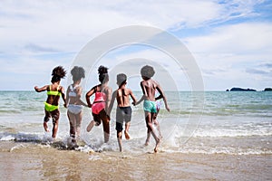 African American, Kids group in swimwear enjoying running to play the waves on beach. Ethnically diverse concept. Having fun after