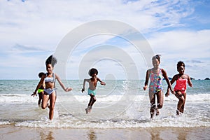 African American, Kids group in swimwear enjoying running to play the waves on beach. Ethnically diverse concept. Having fun after