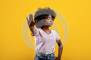 African american lady gesturing STOP, showing rejection gesture on yellow studio background