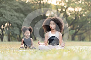 African American little girl sitting on the roll mat practicing meditate yoga in the park outdoor